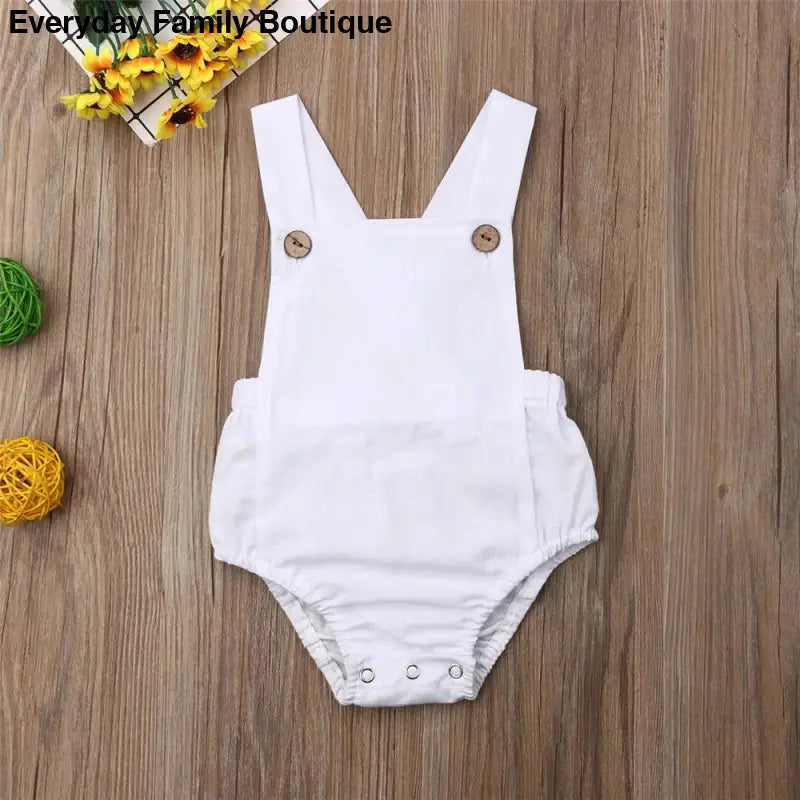 White cotton baby romper with shoulder straps and button closures.