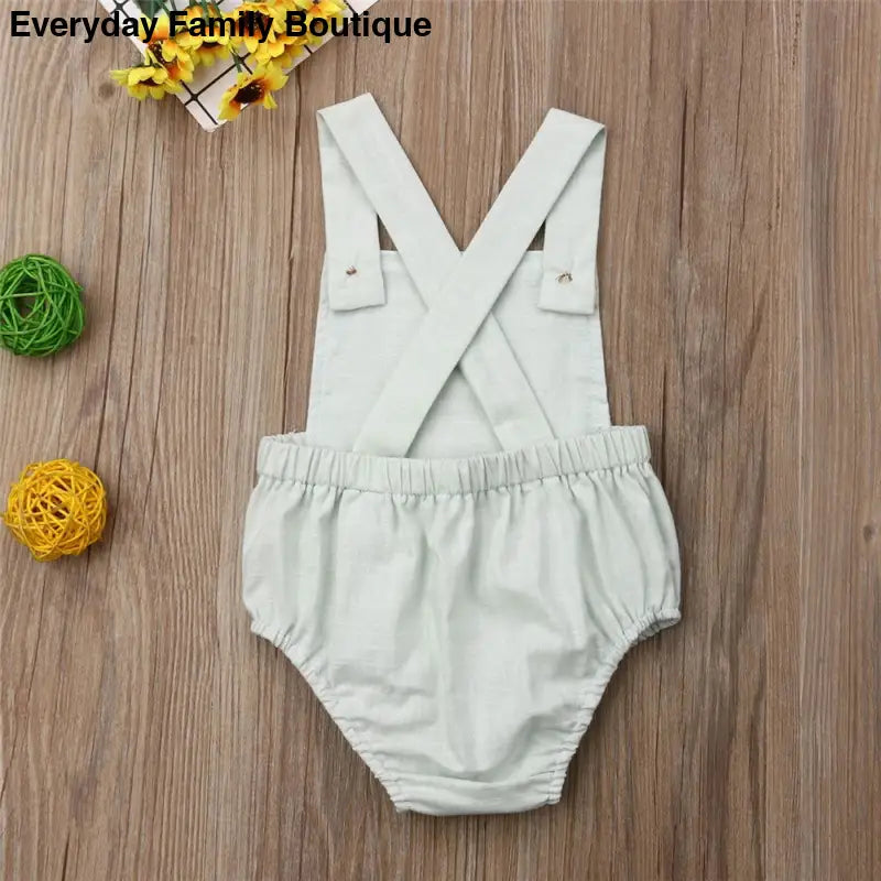 White cotton baby romper with crossed suspender straps.